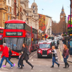 People crossing a street in London in front of red bus