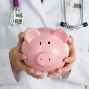Doctor with a stethoscope around neck holding a piggy bank