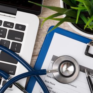 Close-up view of medical doctor’s working table. Laptop stethoscope and patient information form.