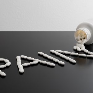 Pain killers spilling from bottle on table. Being in a lot of pain, suffering or relief concept. The word pain written with medicine coming out from package. Writing made with medical products.