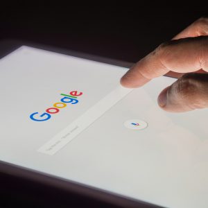 A man's hand is touching screen on tablet at night for searching on Google search engine. Google is the most popular Internet search engine in the world.