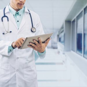 Male doctor working on computer tablet wearing doctors uniform in a hospital or doctors office. Concept of medical data analysis by doctor medical technology and doctors data.